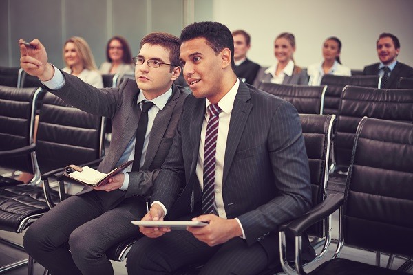 Two businessmen communicating at seminar on background of their colleagues